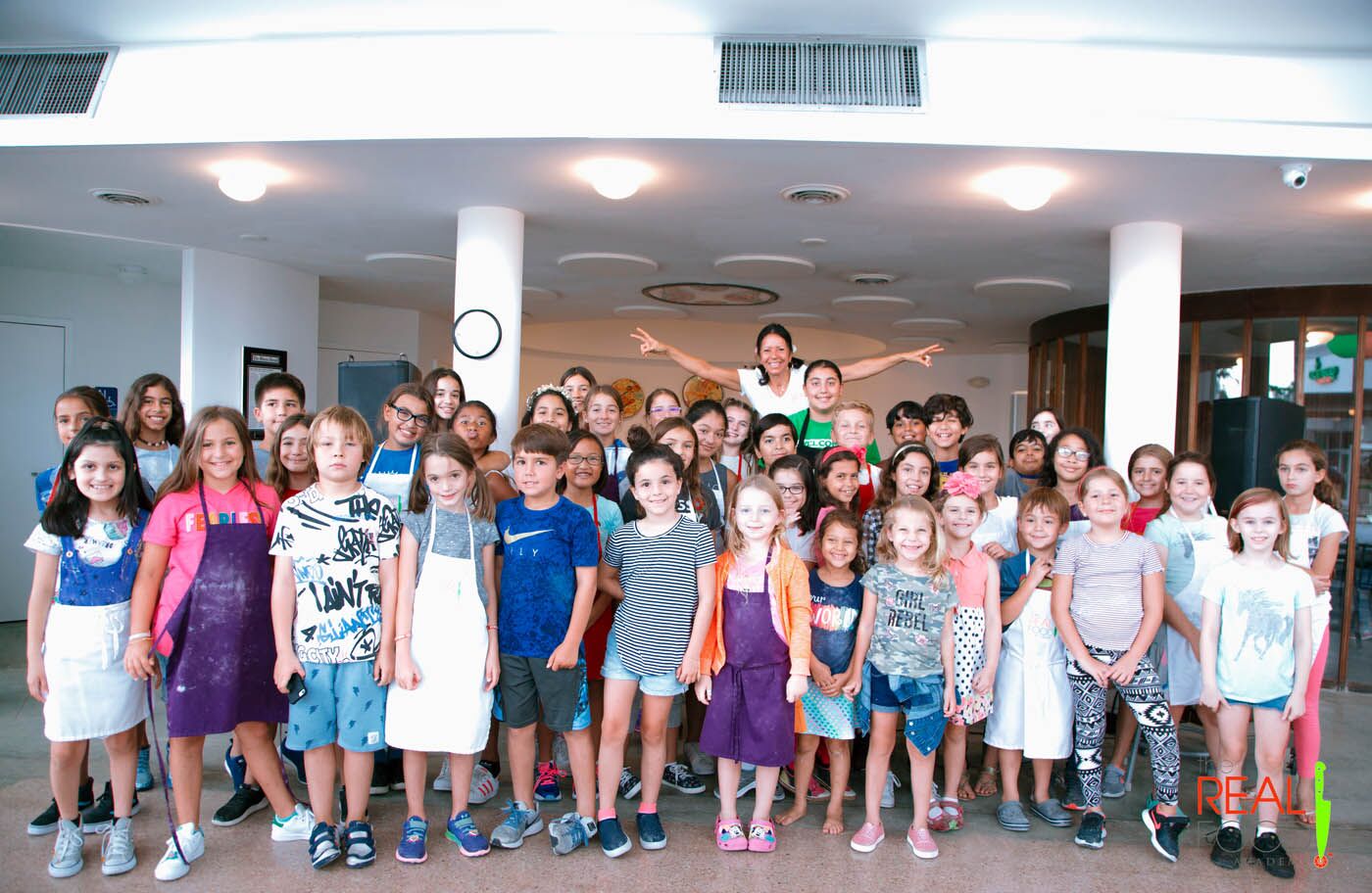 Chef Maria and a group of kids line up to take a photo during their kids cooking camp at The Real Food Academy Miami!