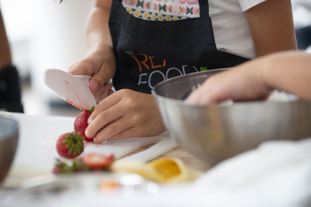 A child cutting a strawberry at The Real Food Academy Miami cooking camp.