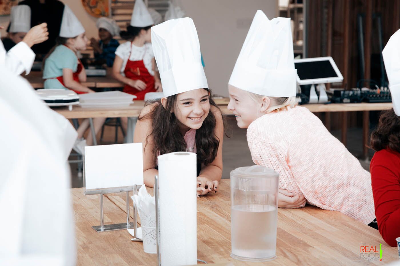 Two young chefs whispering and giggling to each other at a The Real Food Academy Miami cooking camp.