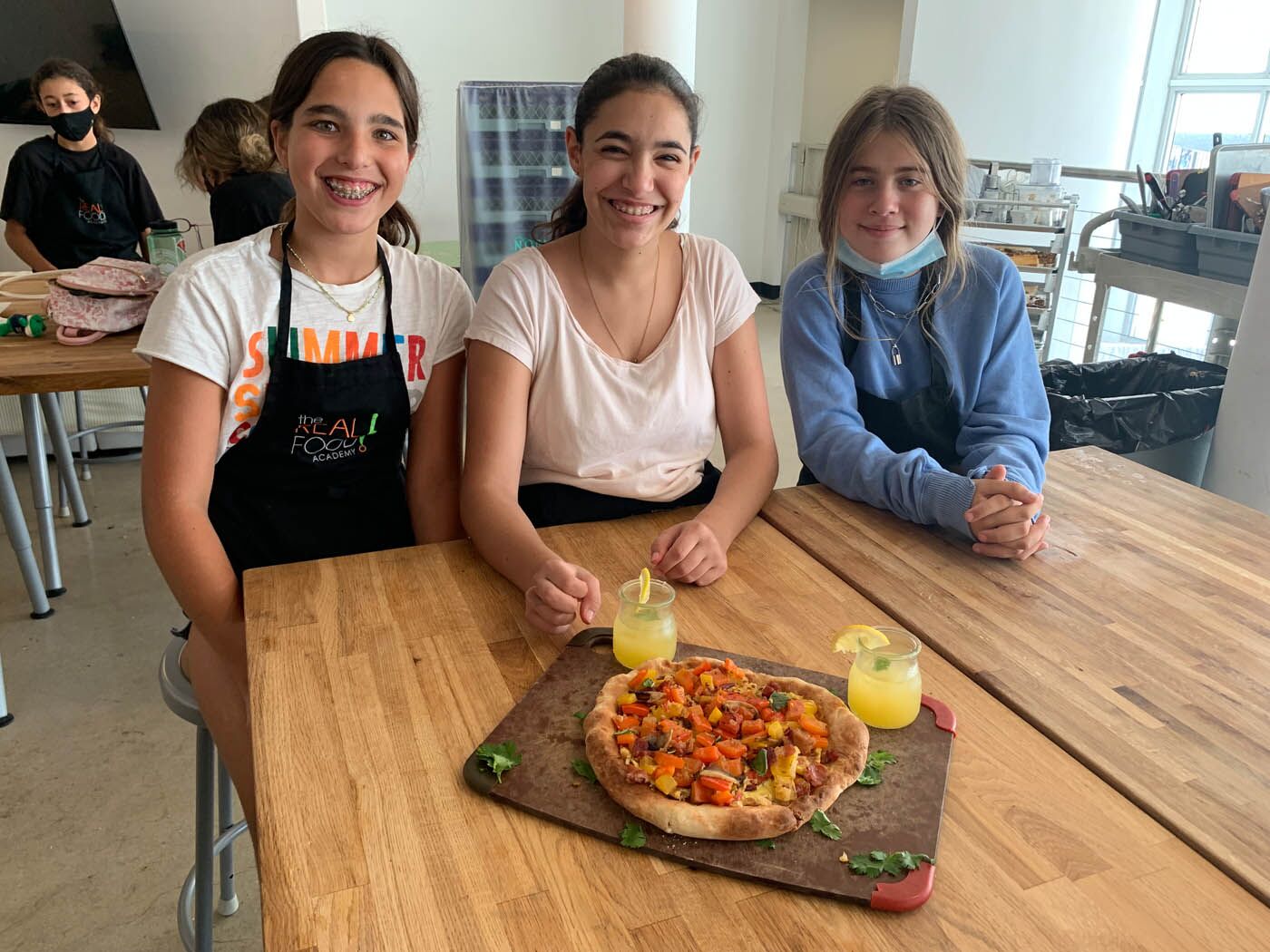 Three girls present a pizza made from wholesome ingredients at a teen The Real Food Academy Miami cooking camp.