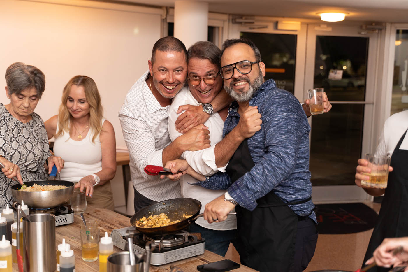 A group of friends hugging and laughing at one of The Real Food Academy's adult cooking classes in Miami, FL.
