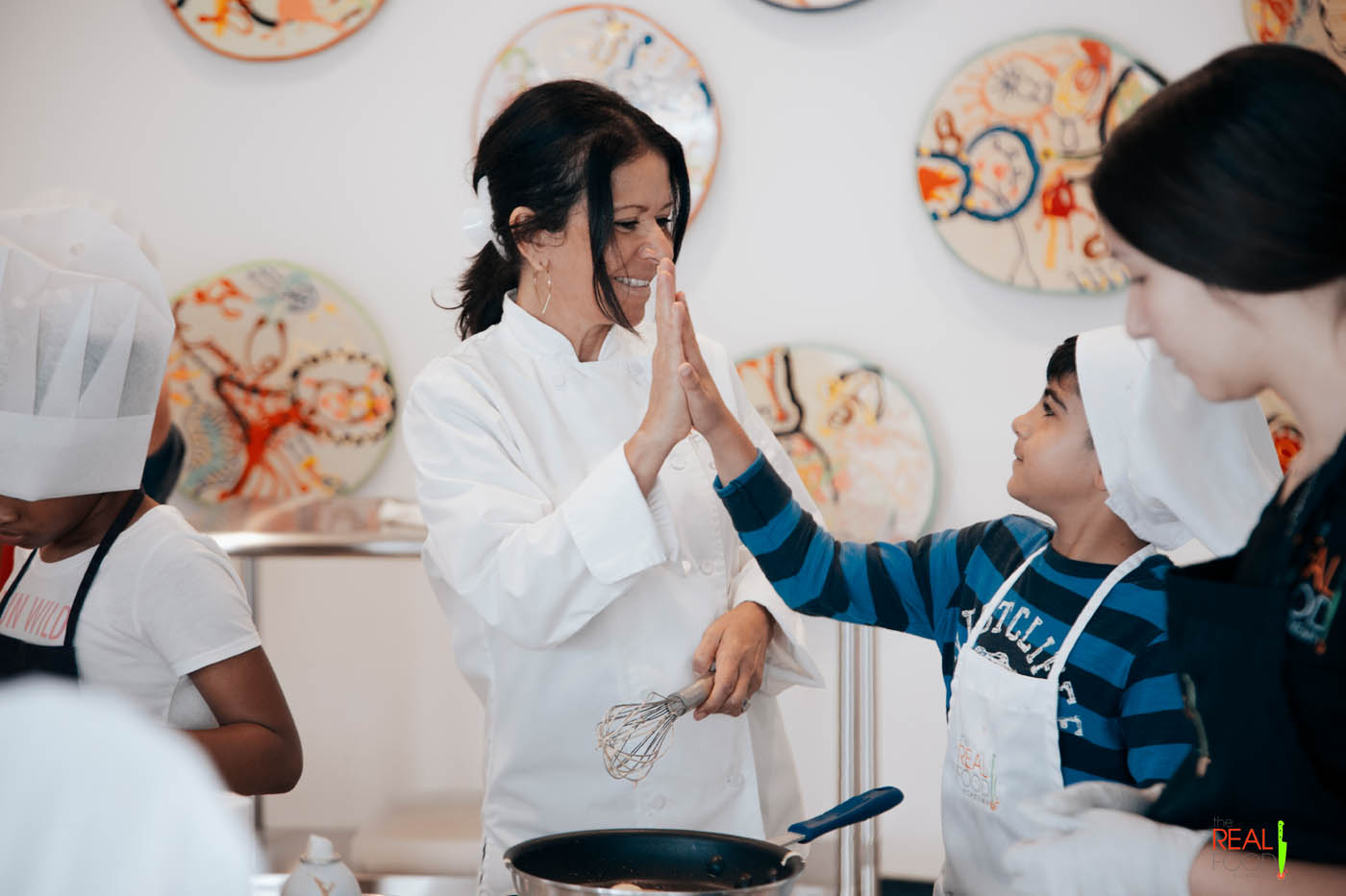 Head chef Maria high fiving a child at The Real Food Academy's kids cooking classes in Miami, FL.