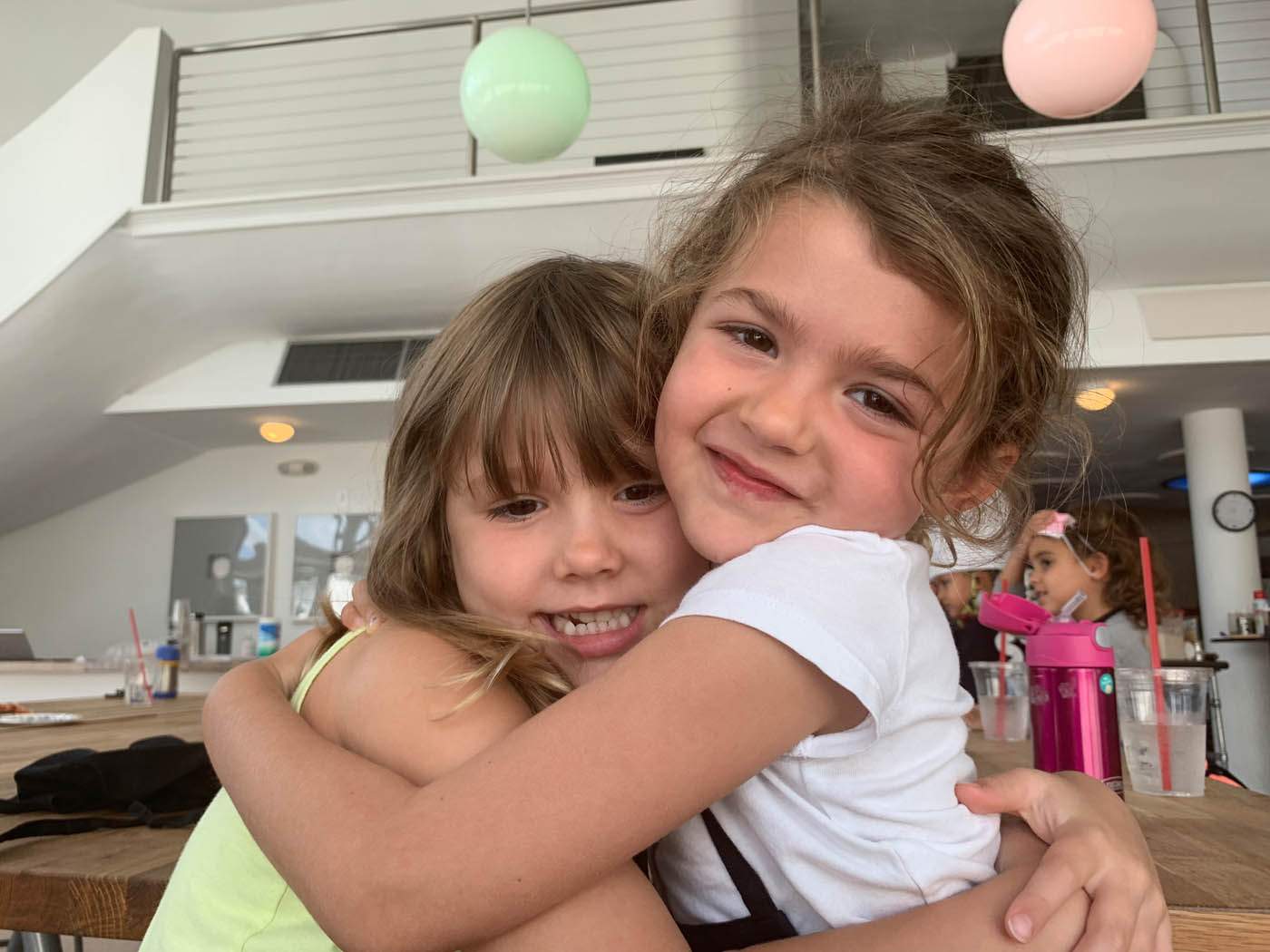 Two young girls hugging at The Real Food Academy's kids and teens cooking class in Miami, FL.