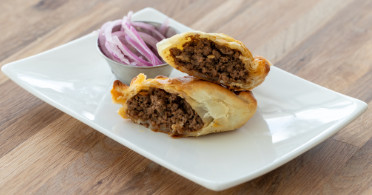 Beef empanadas on a white plate with a side of onions.