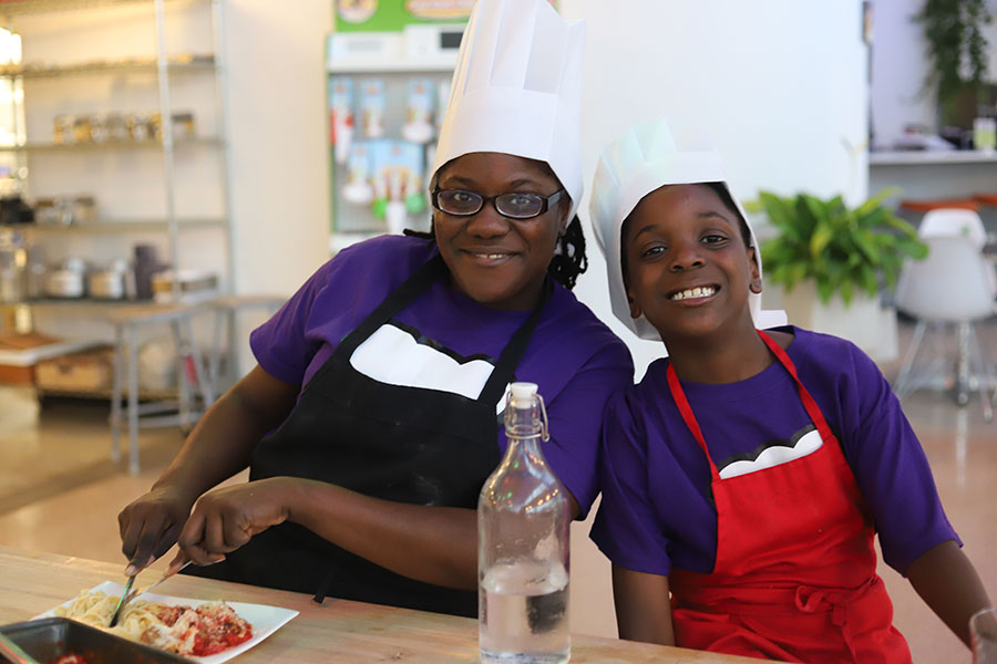 A mom and son in purple shirt participating at one of {fran_brand_names}'s mommy and me cooking classes in Miami, FL.